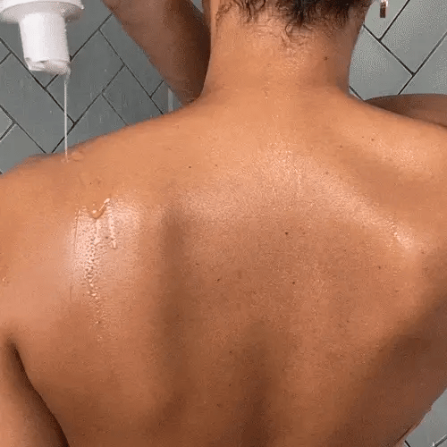 Woman applying exfoliating body wash in the shower