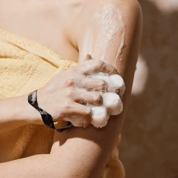 Woman holding exfoliating body wash in a bright bathroom